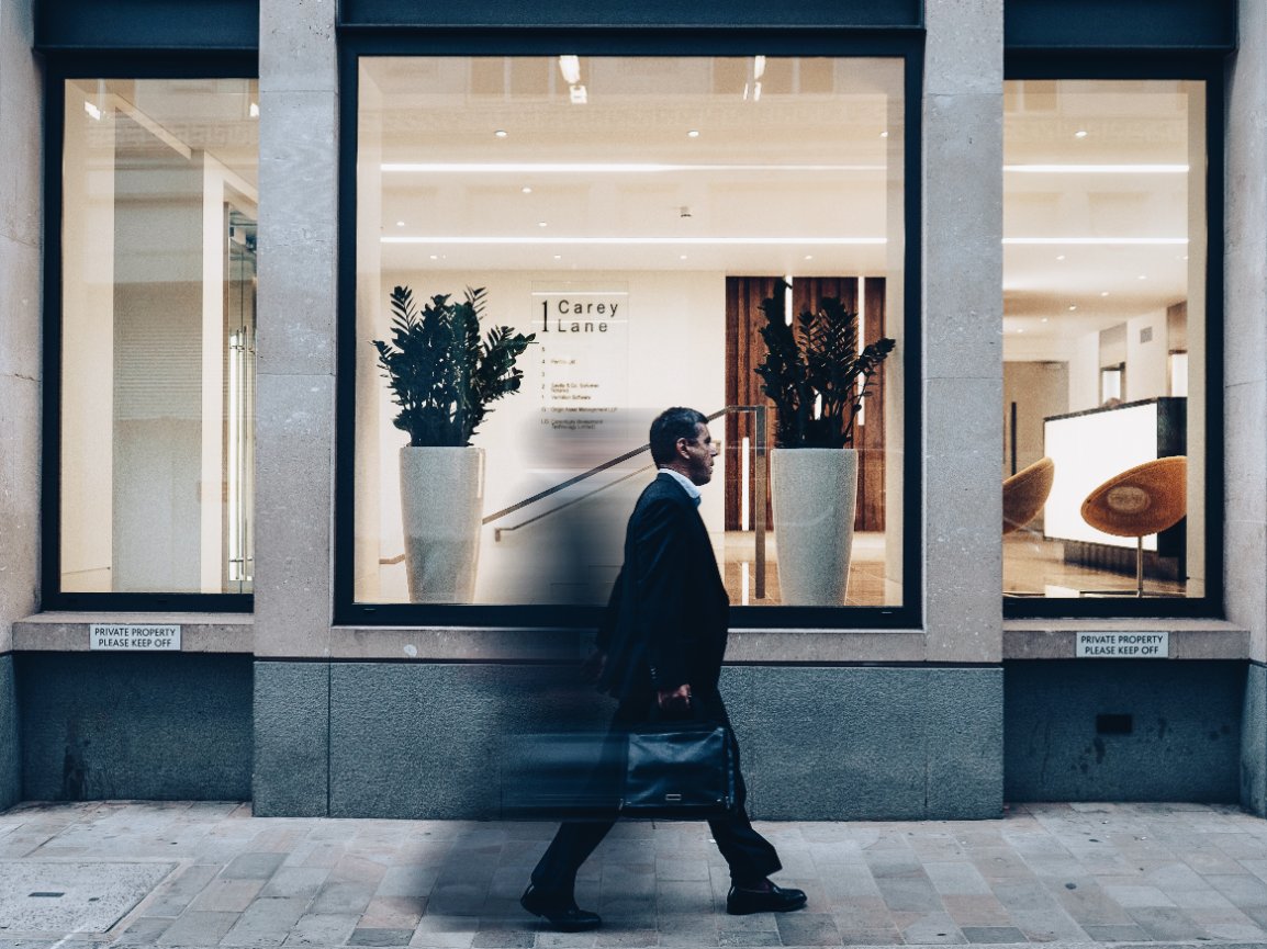 Man walking past a modern storefront with large plants and signage inside.